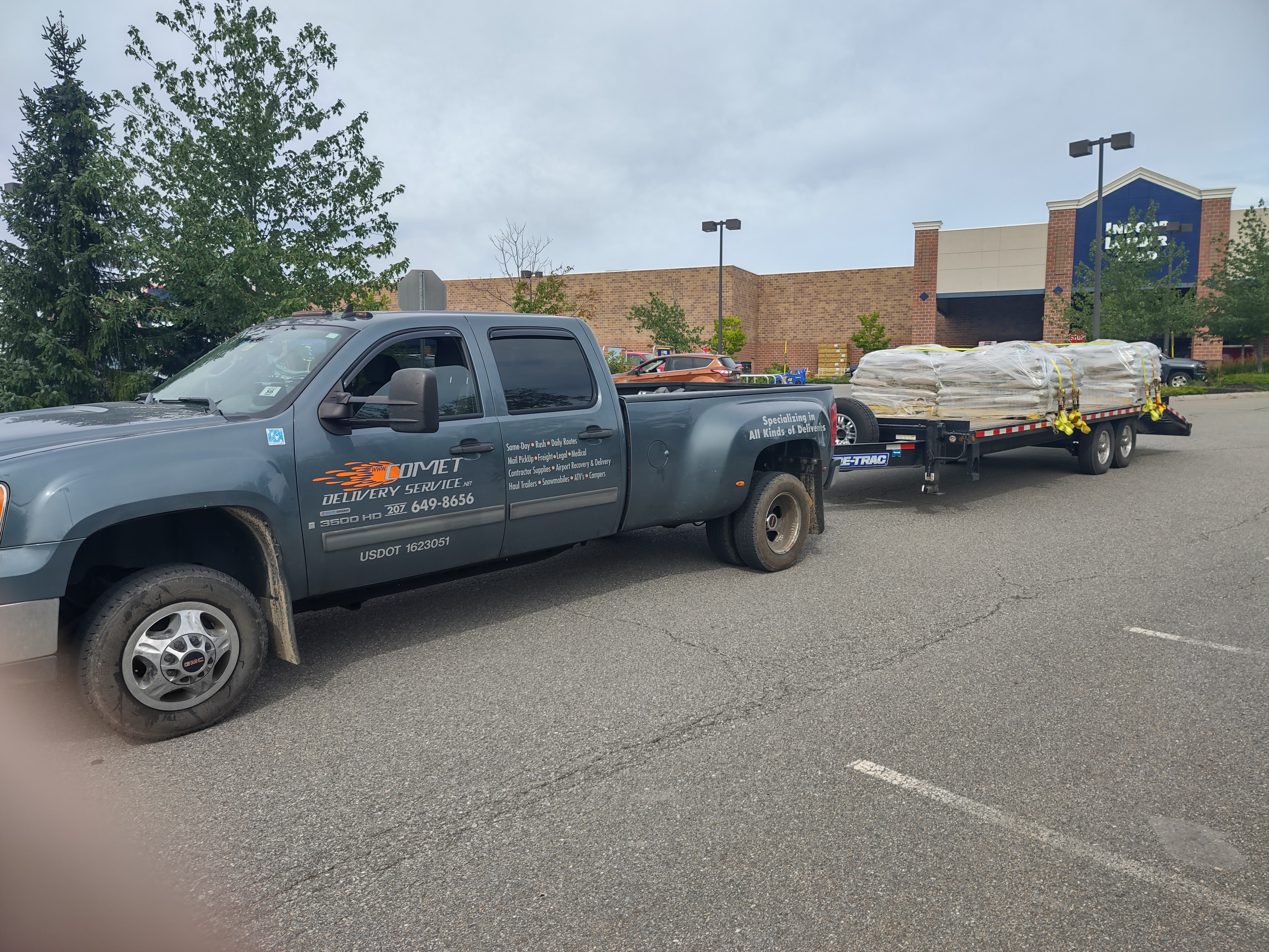Comet Couriers pickup with a loaded equipment trailer at a Maine job site