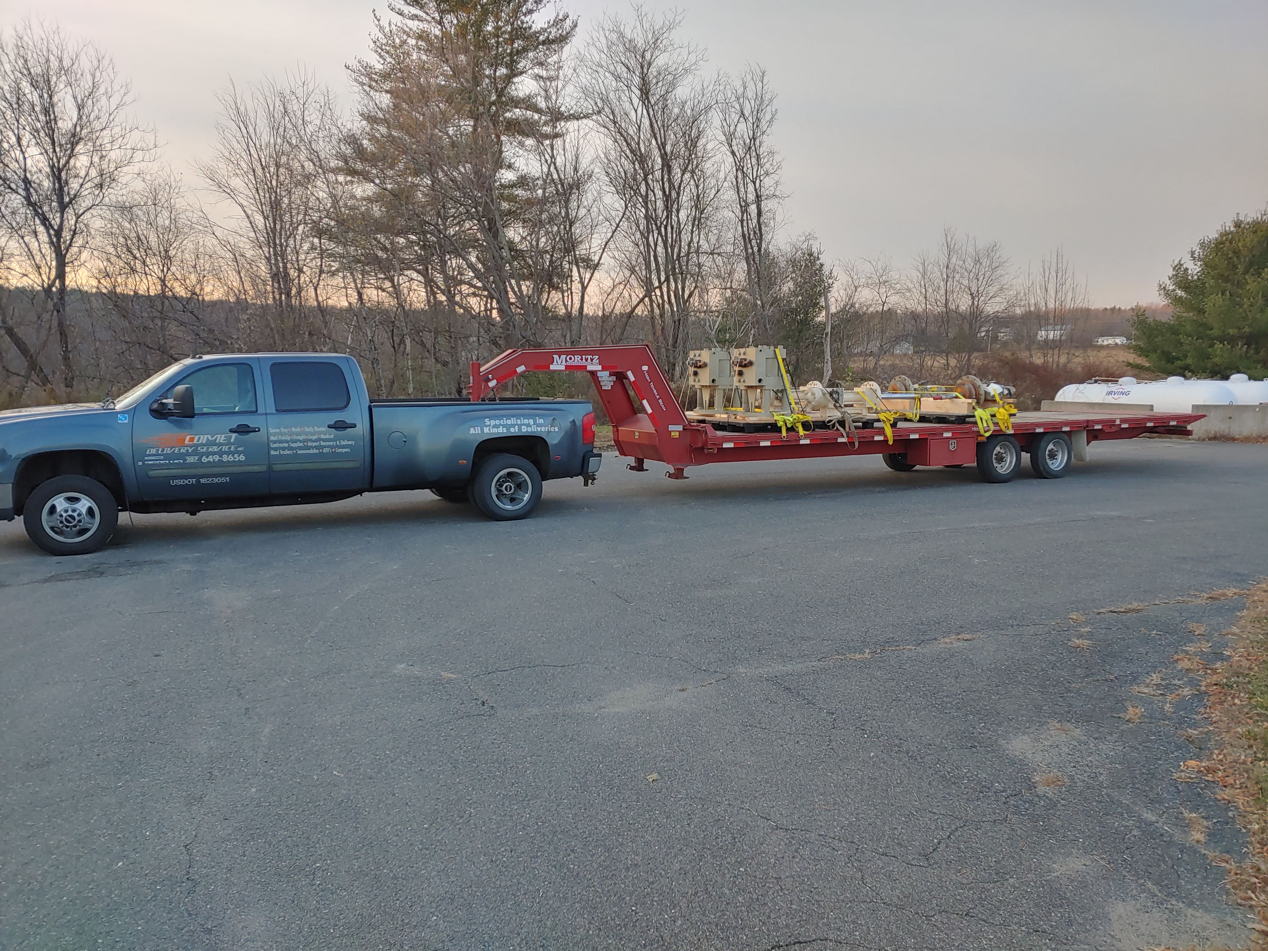 Comet Couriers pickup with a loaded flatbed trailer at dusk