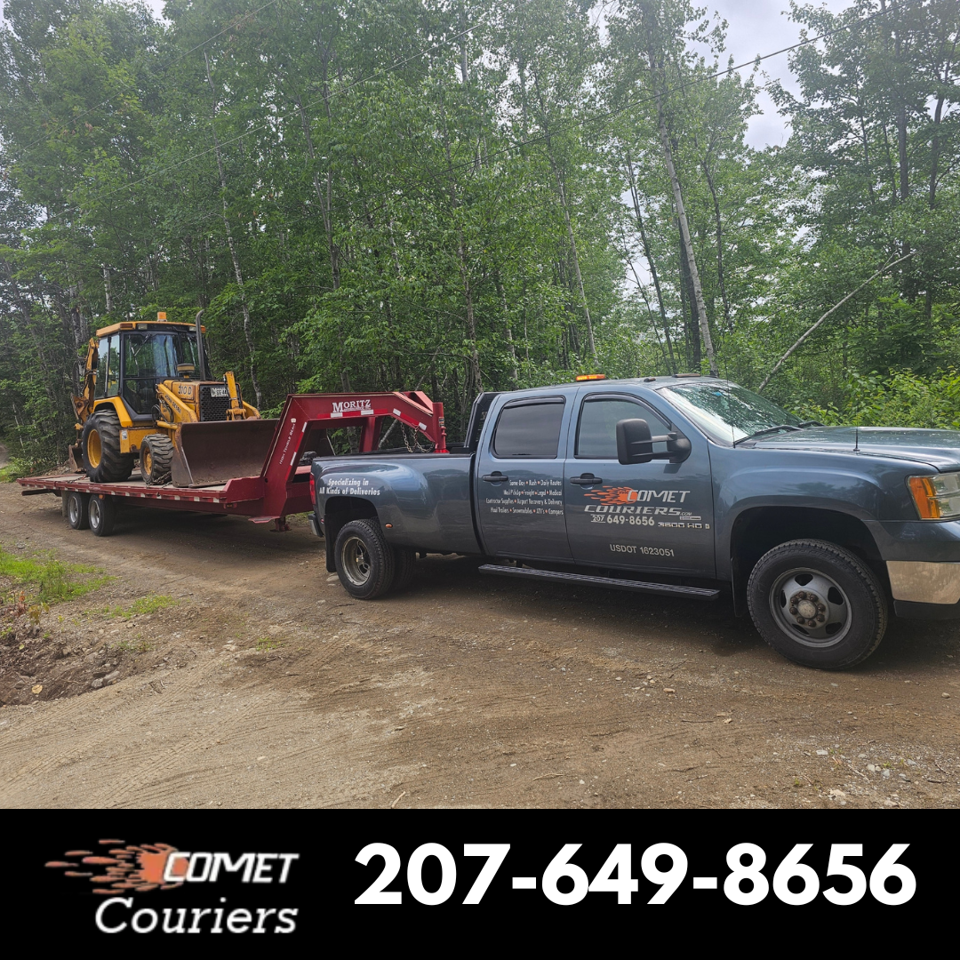 Comet Couriers pickup truck hauling a backhoe on a flatbed trailer through the Maine woods