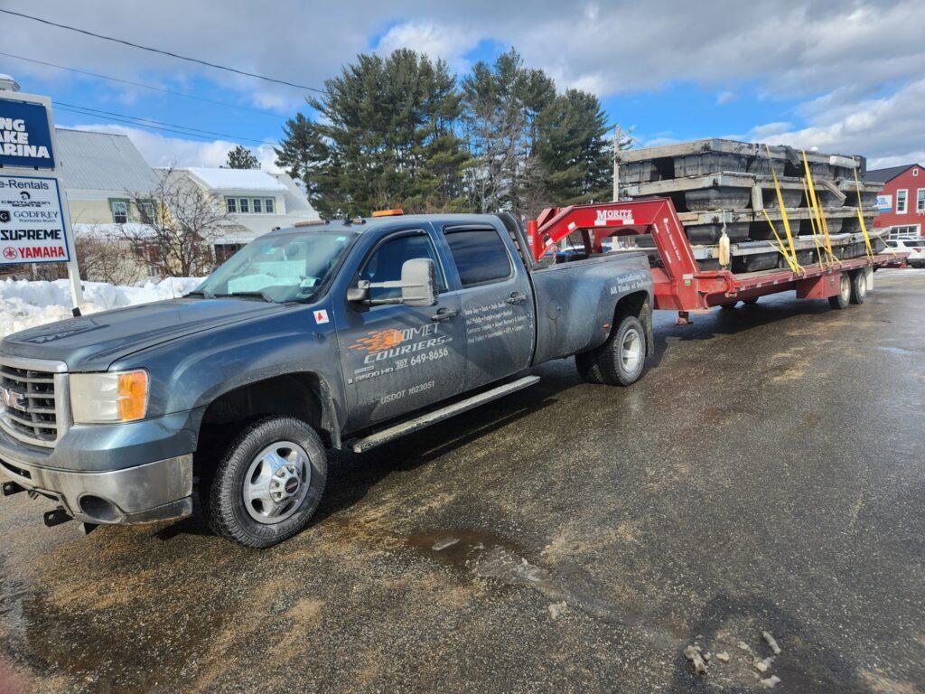Comet Couriers work truck with a flatbed trailer carrying construction equipment