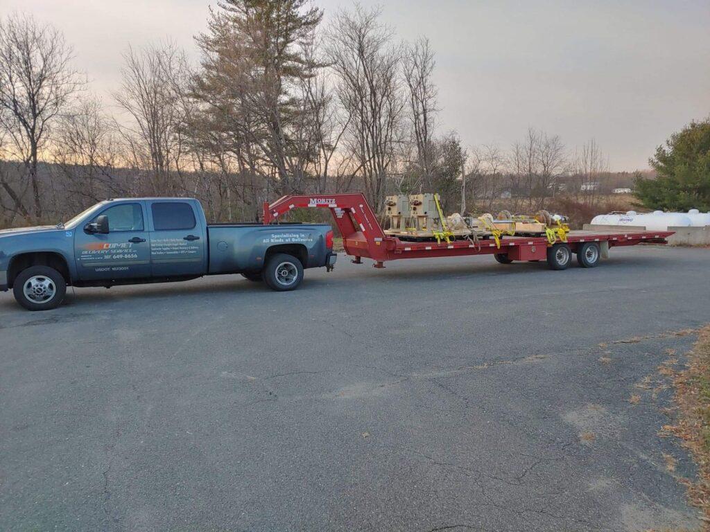 A Comet Couriers heavy duty pickup truck with a flatbed trailer transporting heavy equipment.
